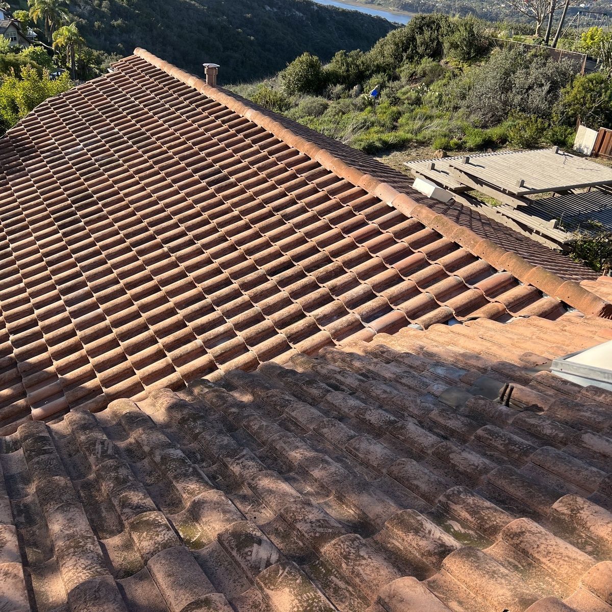 Red tiled roof on a house in a hilly, green landscape under bright sunlight
