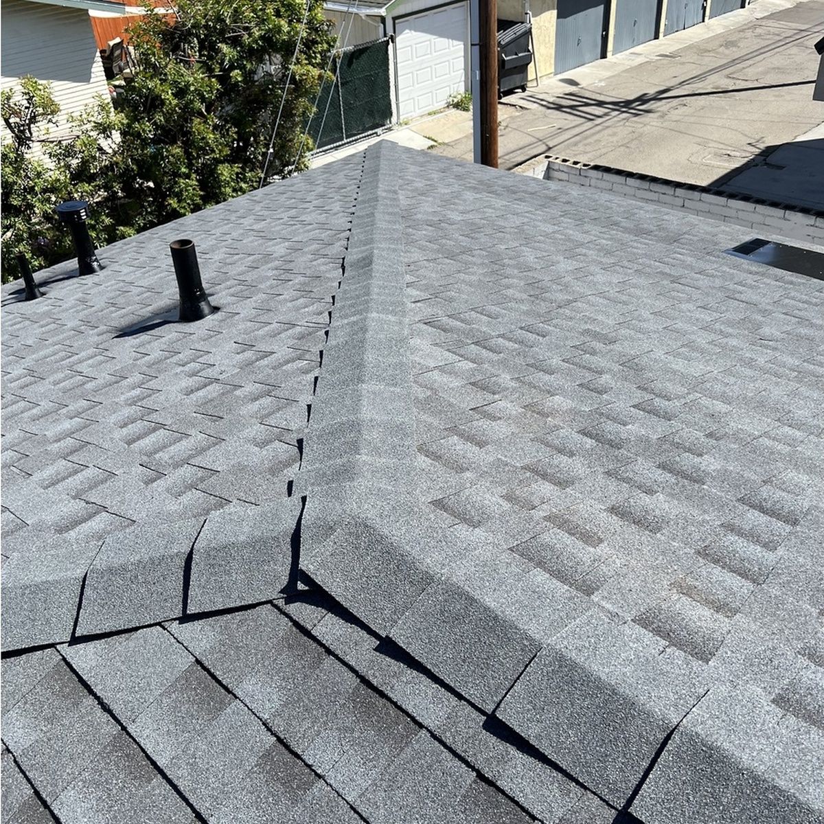 Gray shingled rooftop with vents, viewed from above in a residential area