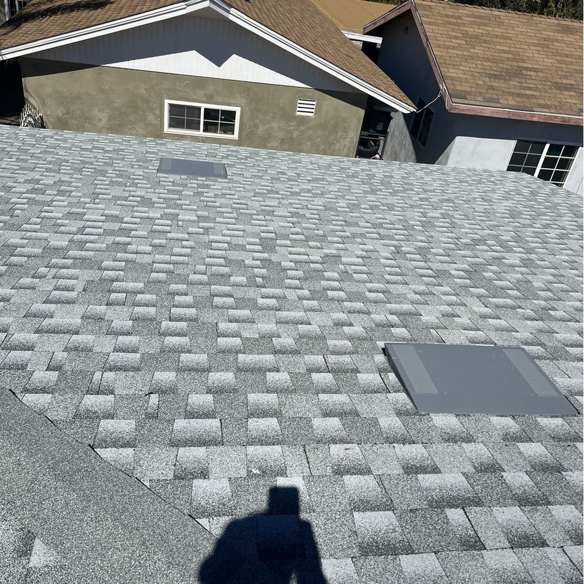 View from a rooftop with gray shingles and a skylight, overlooking neighboring houses.