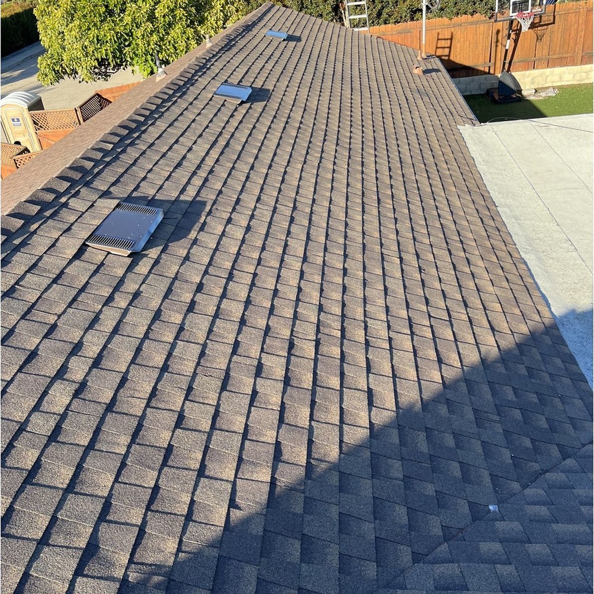 Roof with gray shingles and three skylights, viewed from above in bright sunlight.
