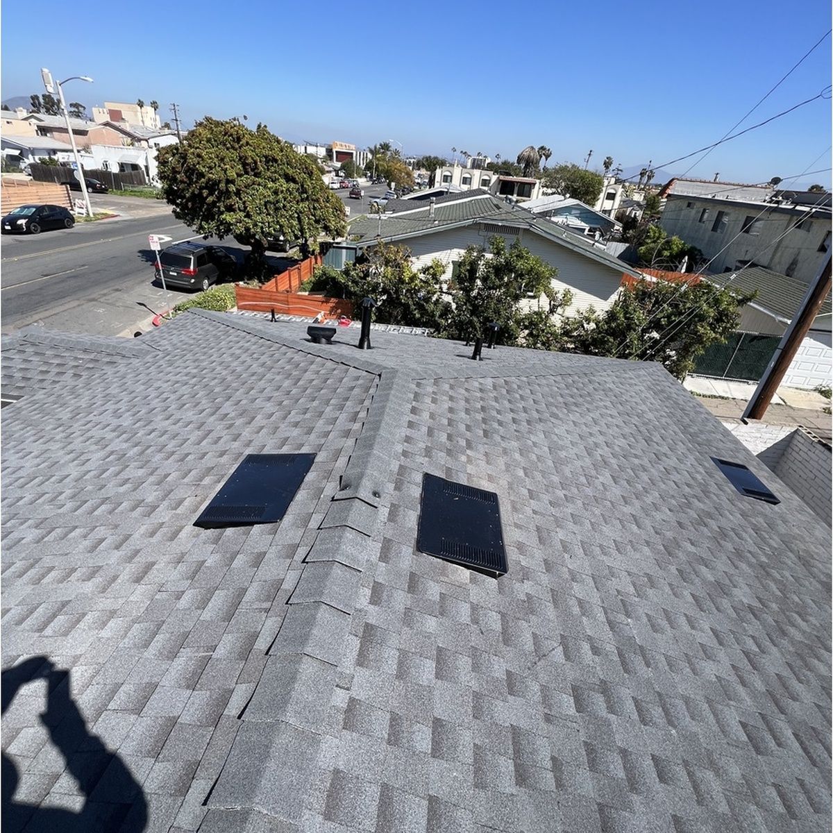 Rooftop with gray shingles and skylights overlooking a sunny suburban neighborhood