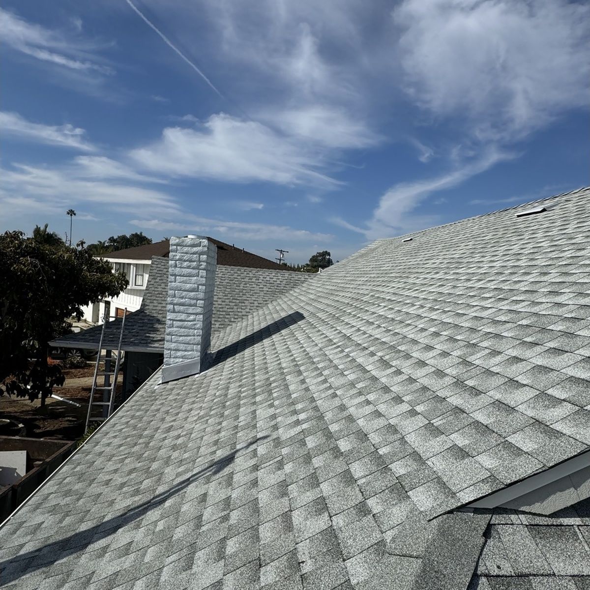 Gray shingled roof with chimney under a blue sky with wispy clouds