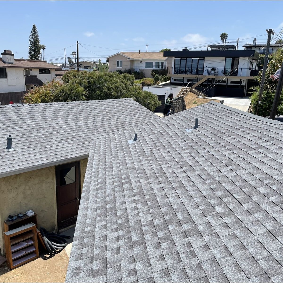 Gray shingled rooftops in a residential neighborhood under a clear blue sky
