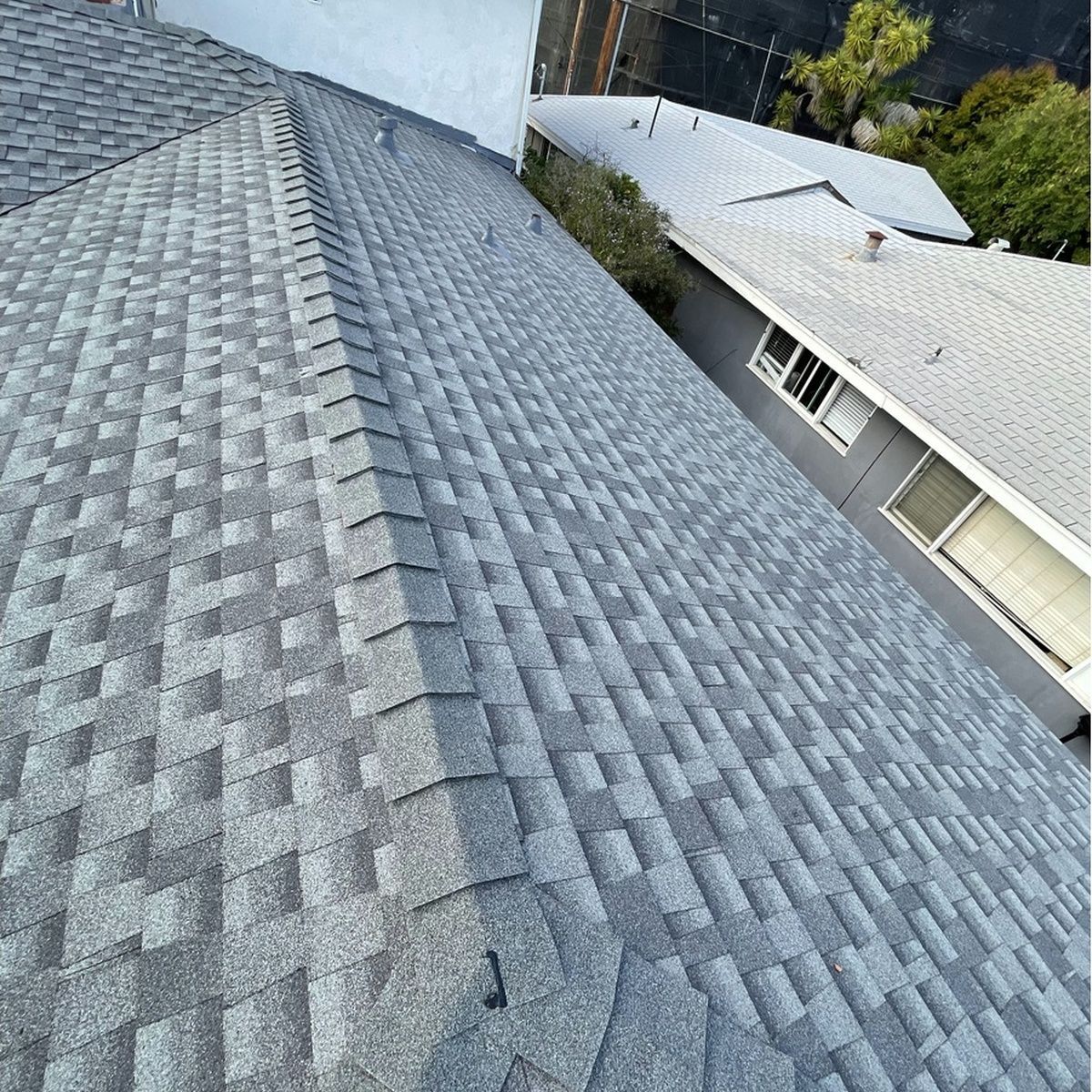 Gray shingled rooftop viewed from above, with a neighboring house and trees in the background