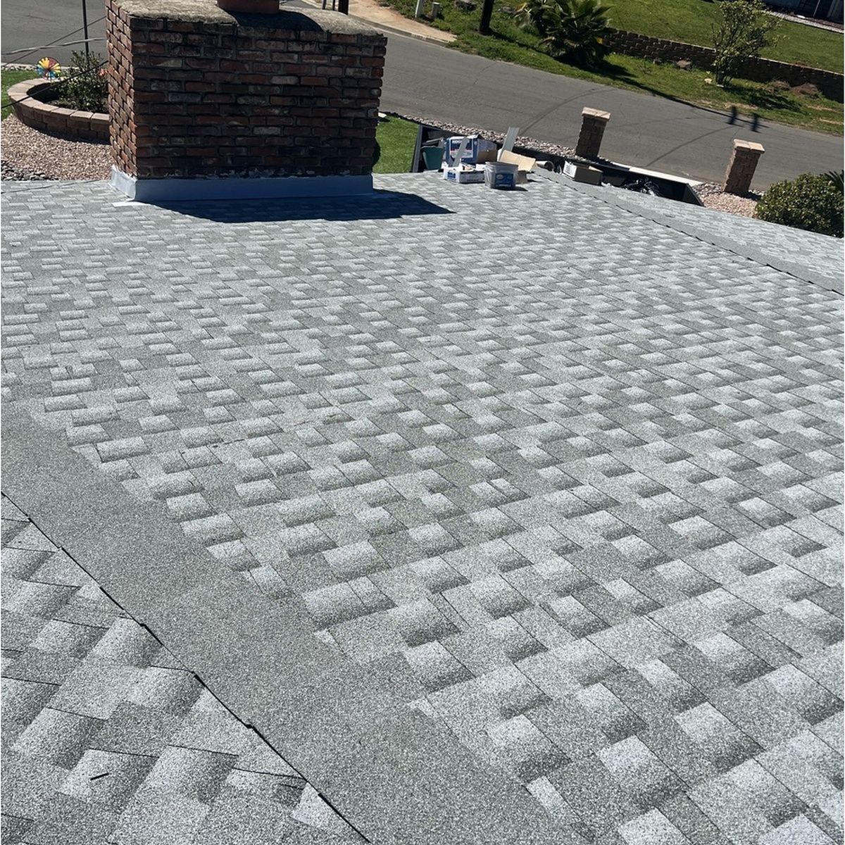 Gray patterned shingle roof with a brick chimney and rooftop vents in sunlight
