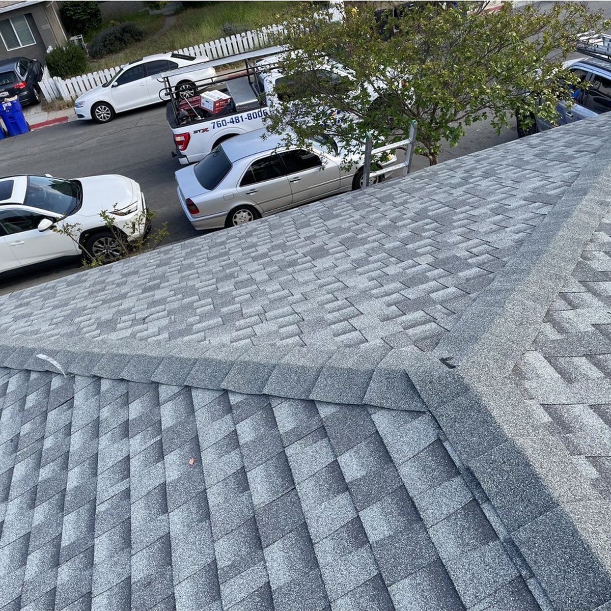 Gray shingled roof overlooking a street with parked cars and a few people near trees