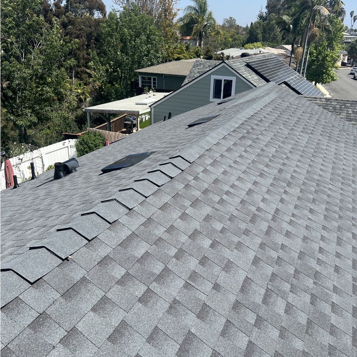 Gray shingled roof with skylights and rooftop vents in a leafy residential neighborhood