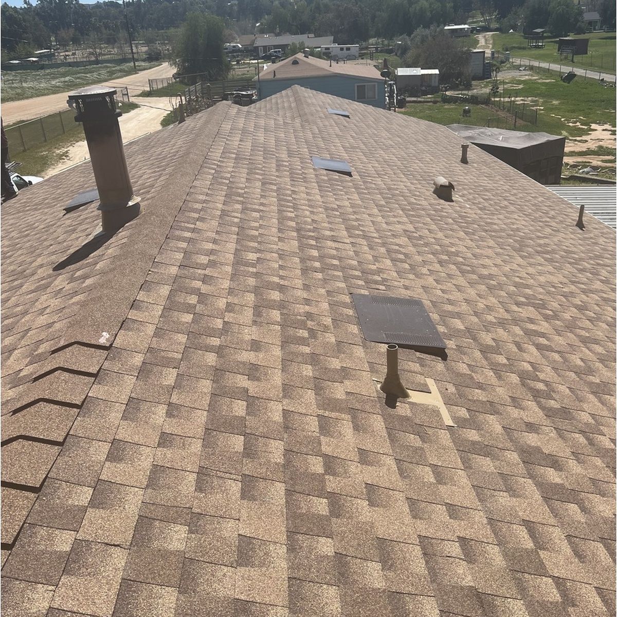 Shingled rooftop with vents and chimneys under a bright sky, viewed from the ridge line.