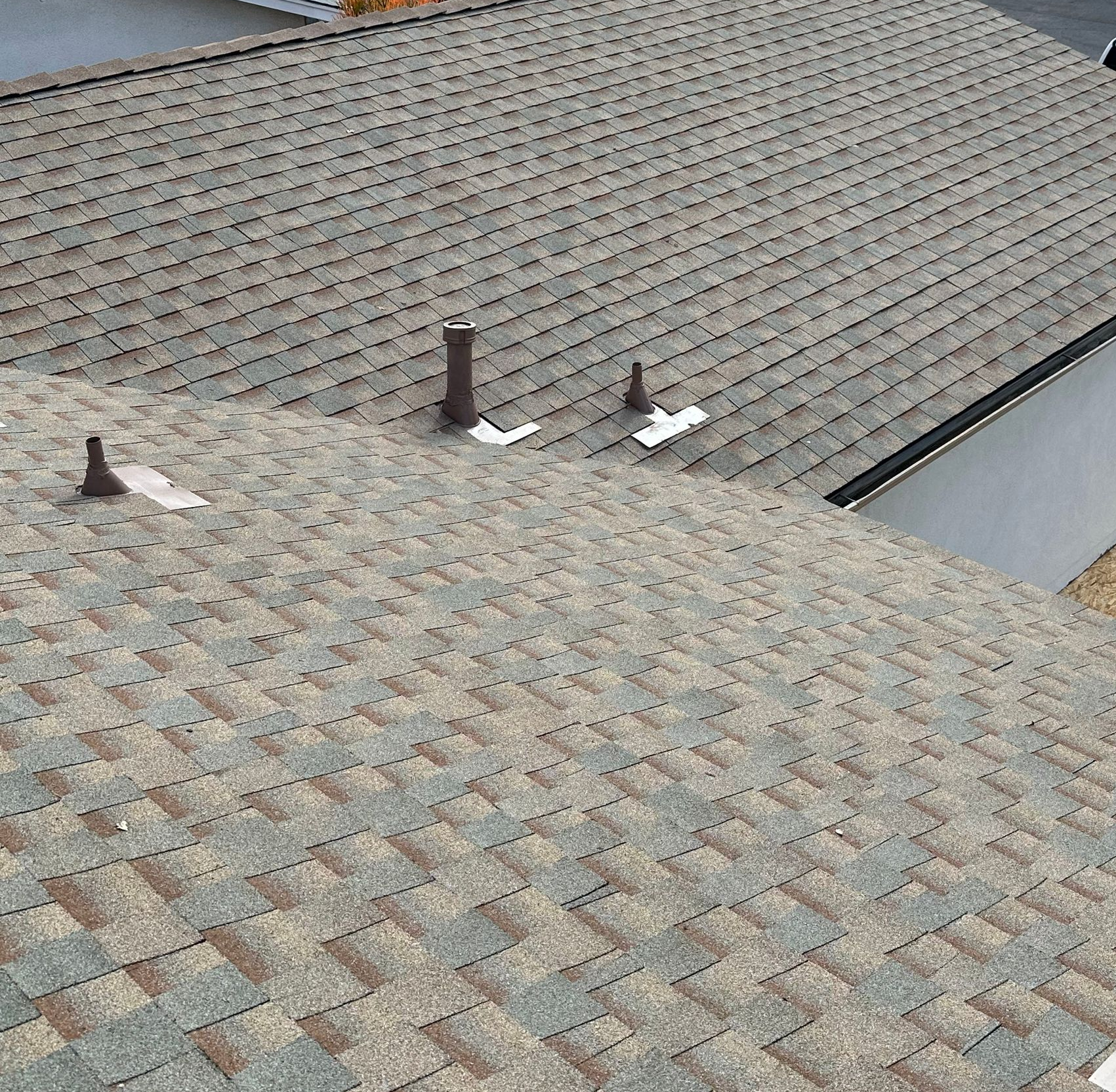 Workers repairing a shingled roof, with stacked GAF shingles and tools on a cloudy day.
