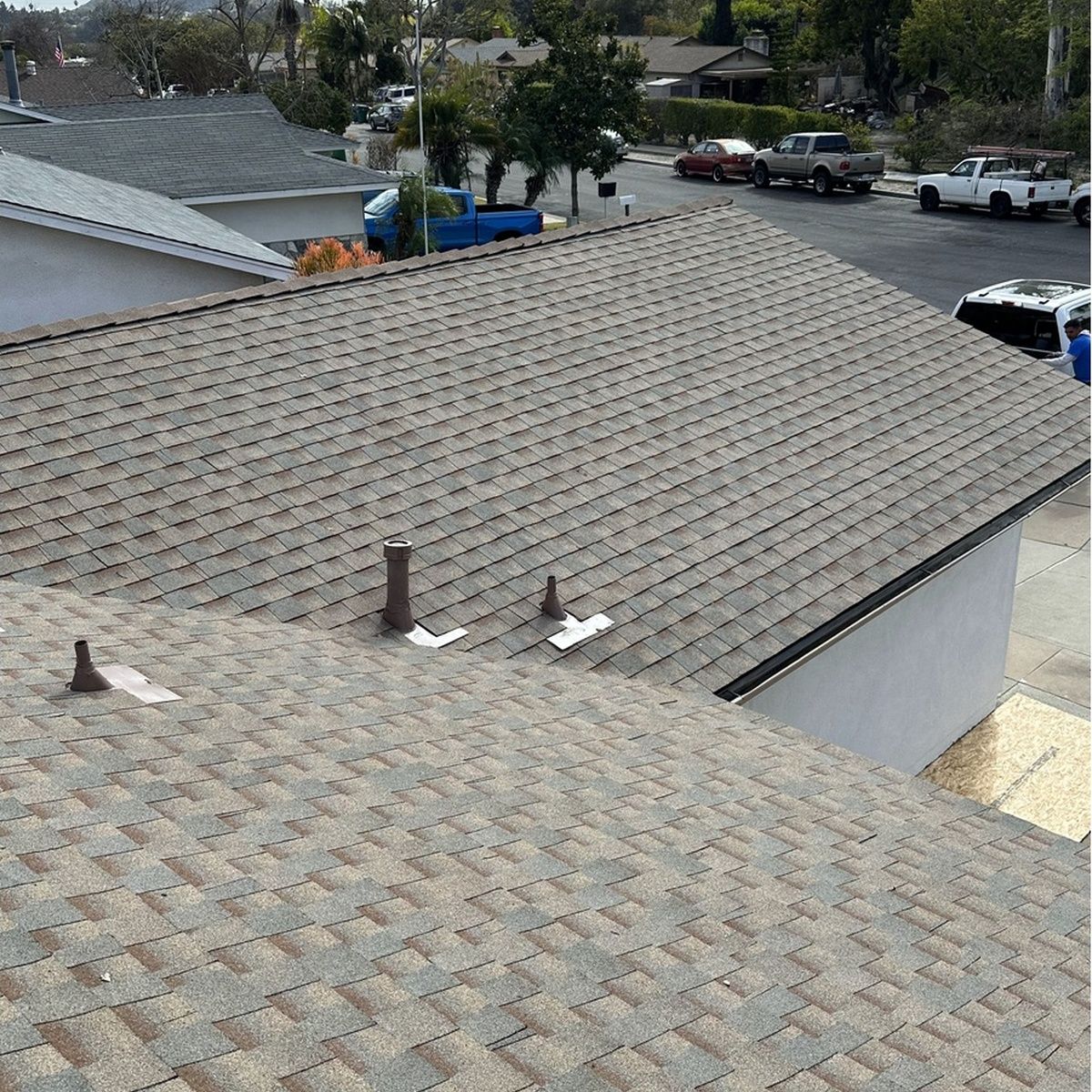 Two shingled rooftops with roof vents, viewed from above in a suburban neighborhood.