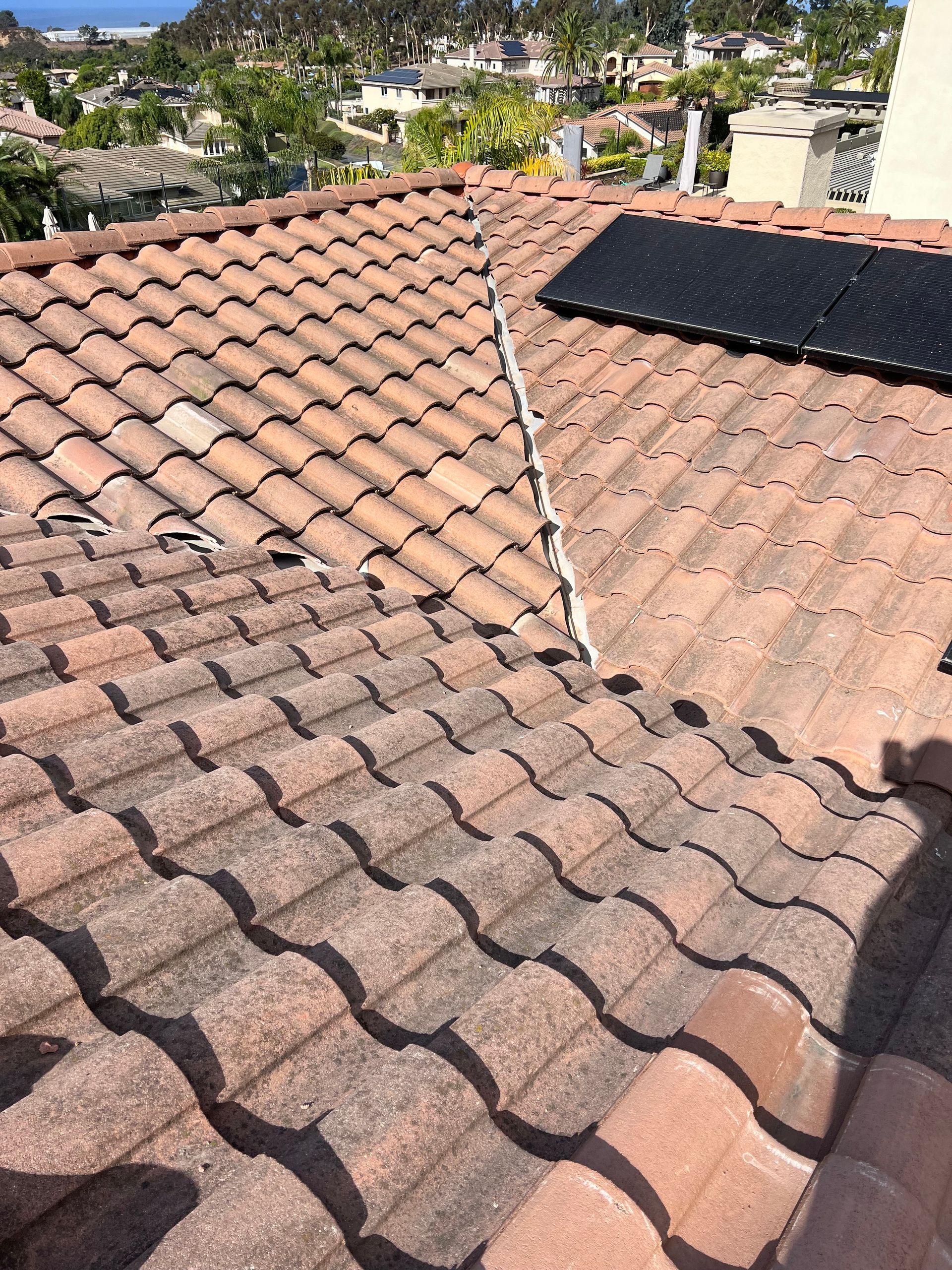 Rooftop with weathered red clay tiles and a black solar panel under a clear sky.