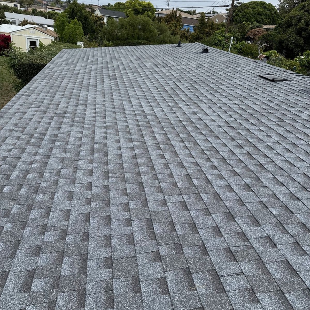 Gray shingled rooftop seen from above, with trees and buildings in the background