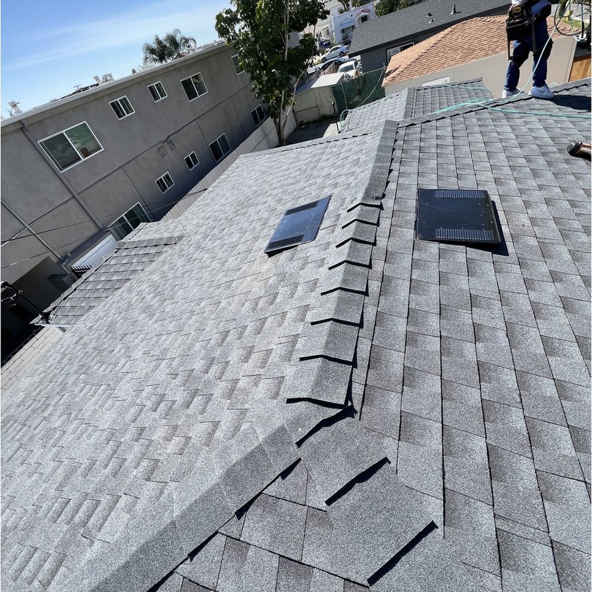 Roof with gray shingles, two skylights, and workers near the ridge on a sunny day