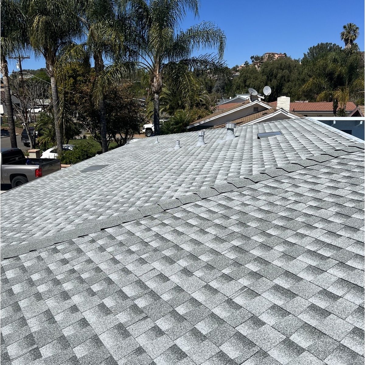 New gray shingle roof with palm trees and houses in the background