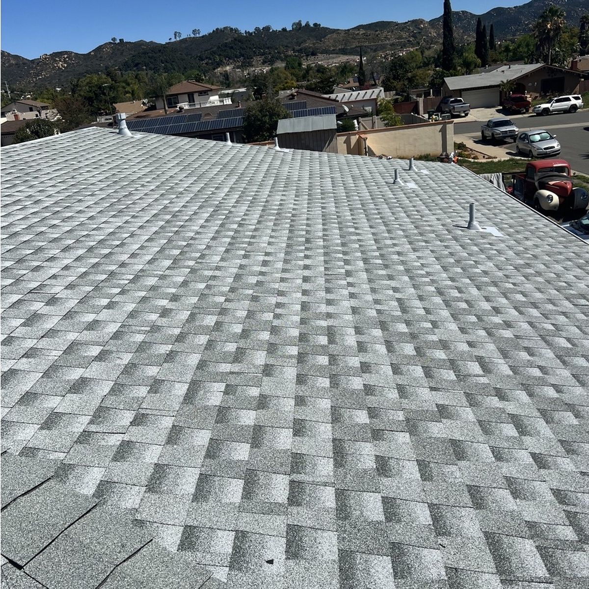 Gray shingled rooftop with a vent, overlooking houses and hills on a sunny day