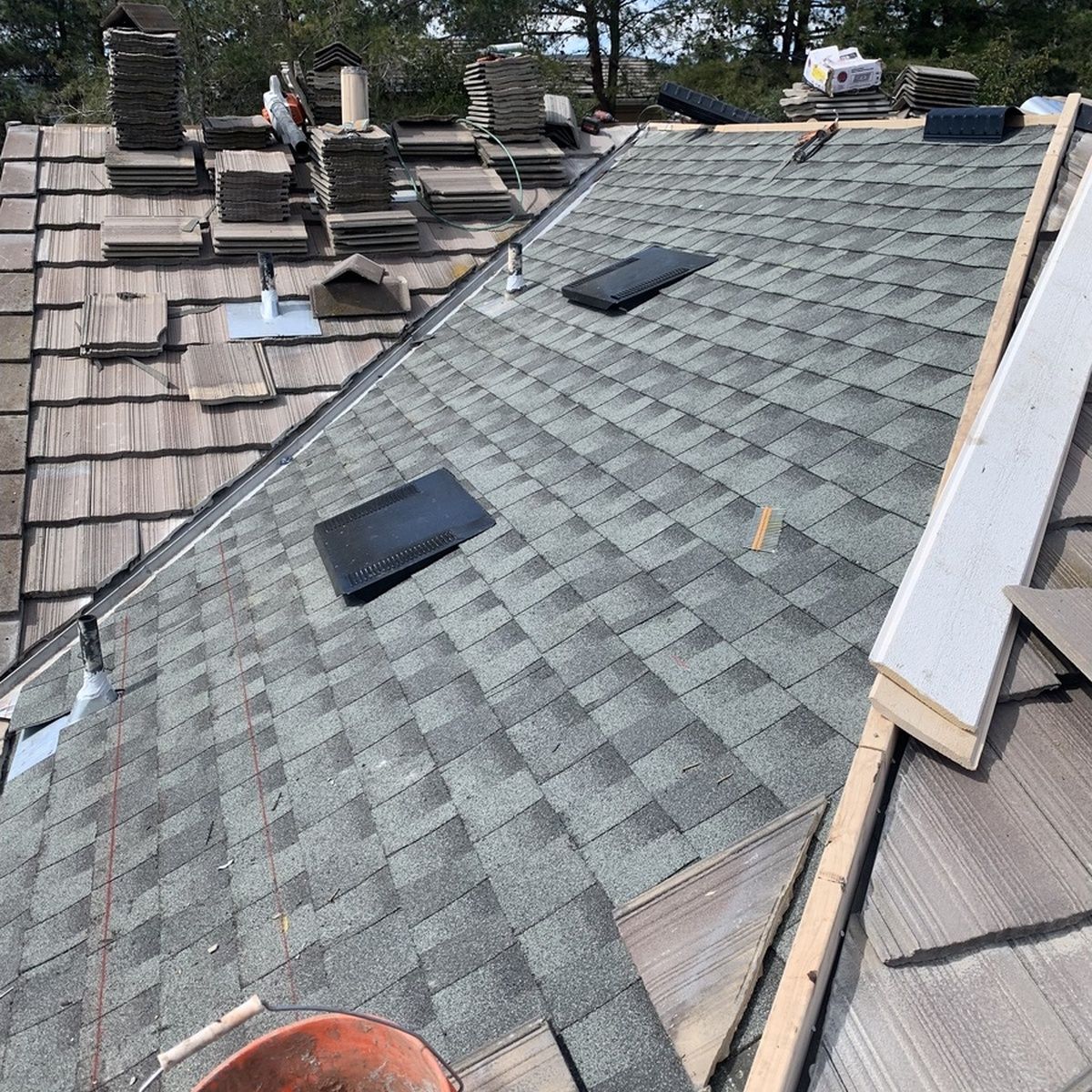 Roof under repair with green shingles, two skylights, and visible roofing materials and tools.