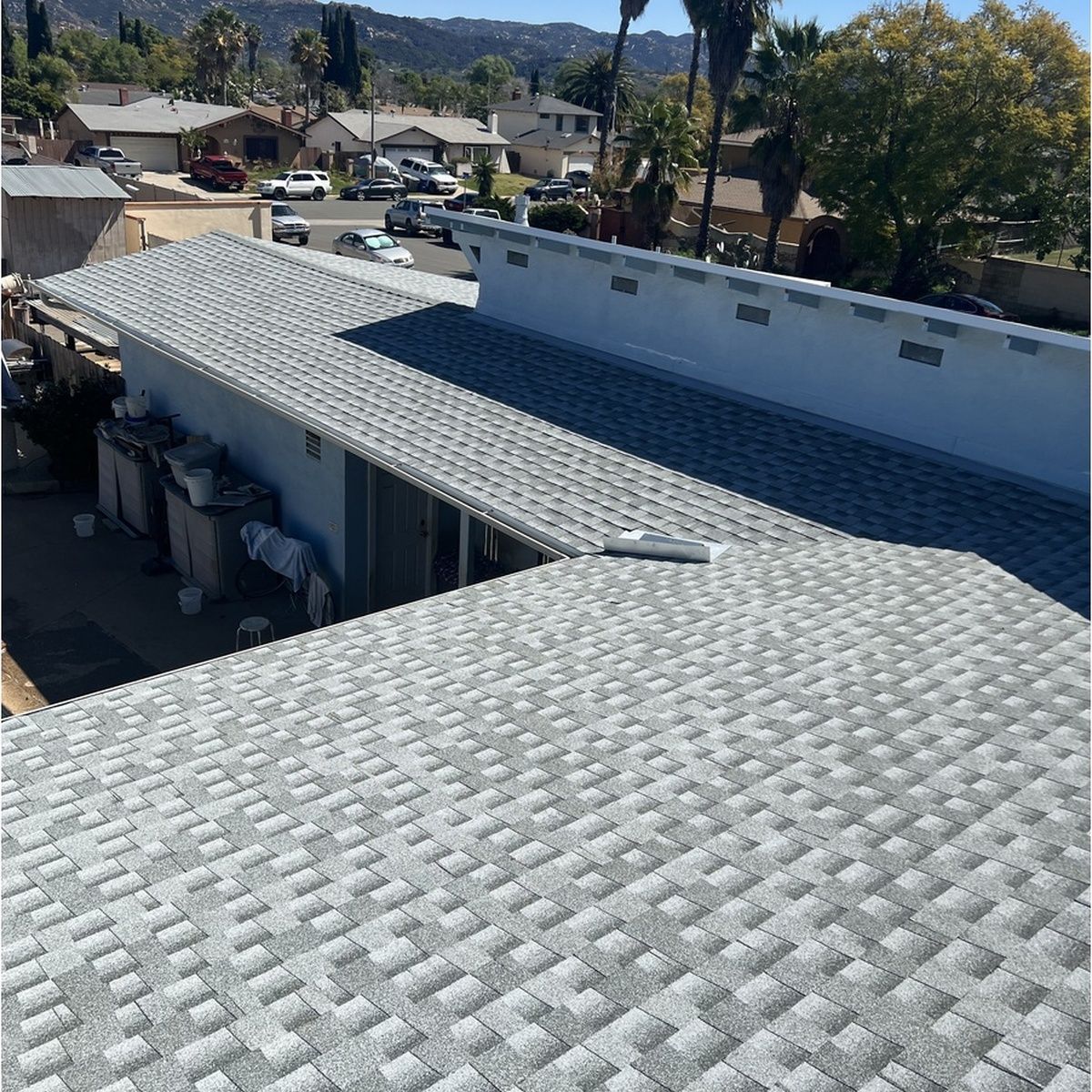View from a rooftop of gray shingle roofs and a suburban street with houses and trees.