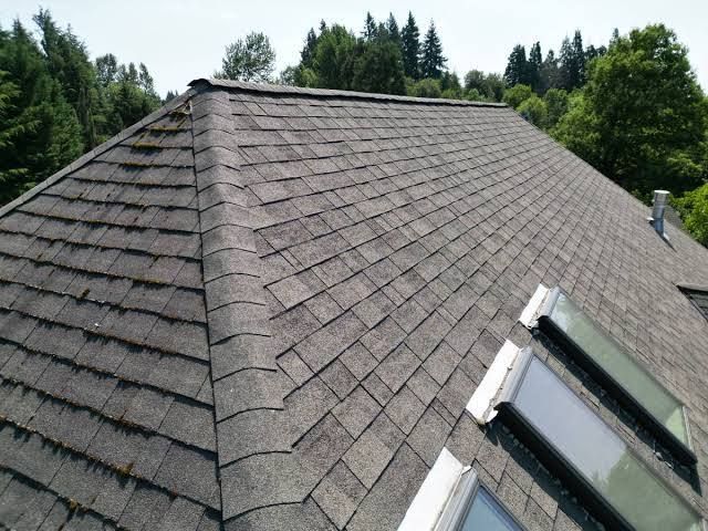 Worker in orange hard hat inspecting roof shingles beside a wall