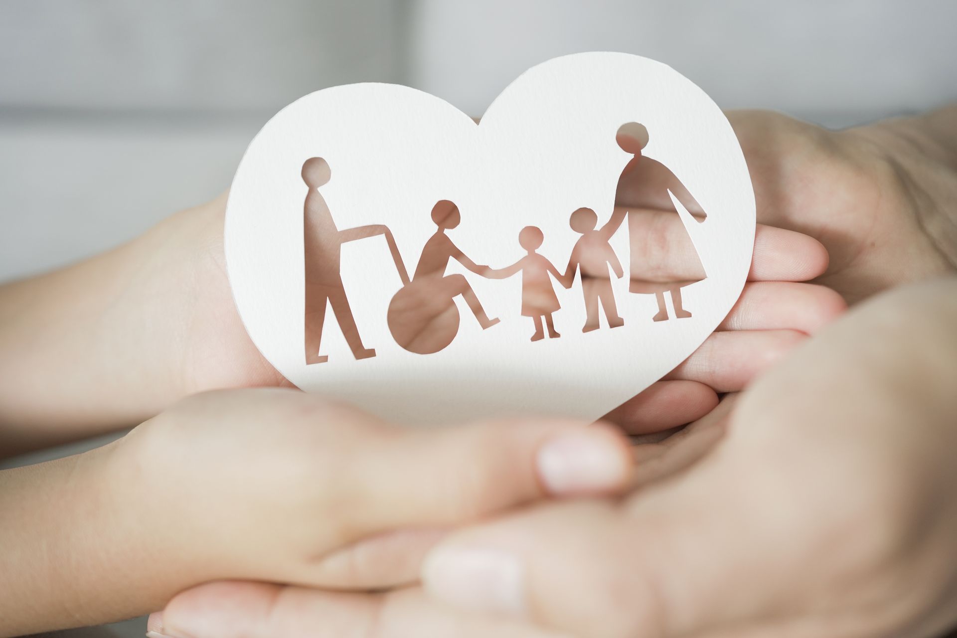 Paper cutout family holding hands inside a white heart over clasped hands