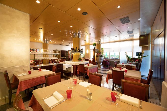 Una sala da pranzo con pareti in blocchi di cemento bianchi e travi in legno a vista, arredata con un tavolo per otto persone e sedie marroni.