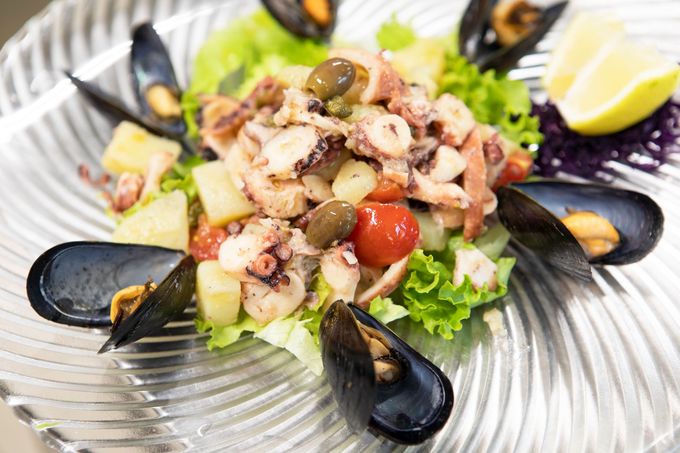 Insalata di mare con cozze, calamari, lattuga, pomodori e spicchi di limone su un piatto di vetro.