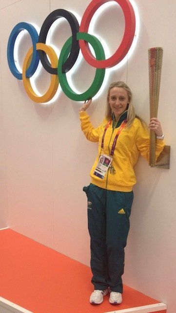 A woman in a yellow jacket is holding a torch in front of the olympic rings