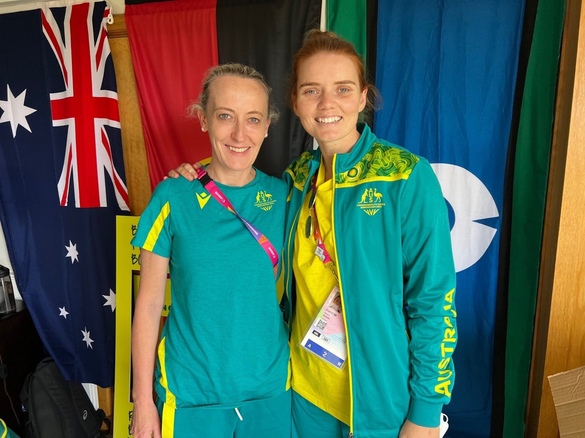 Two women are posing for a picture in front of flags.