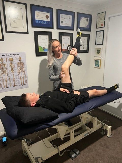 A woman is stretching a man 's leg on a table