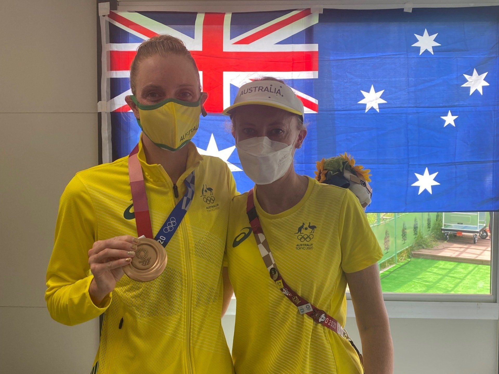 Two people wearing masks are standing next to each other in front of a flag.