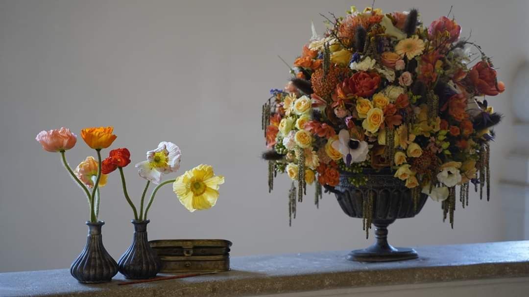 Eine mit Blumen gefüllte Vase steht auf einem Tisch neben zwei weiteren mit Blumen gefüllten Vasen.