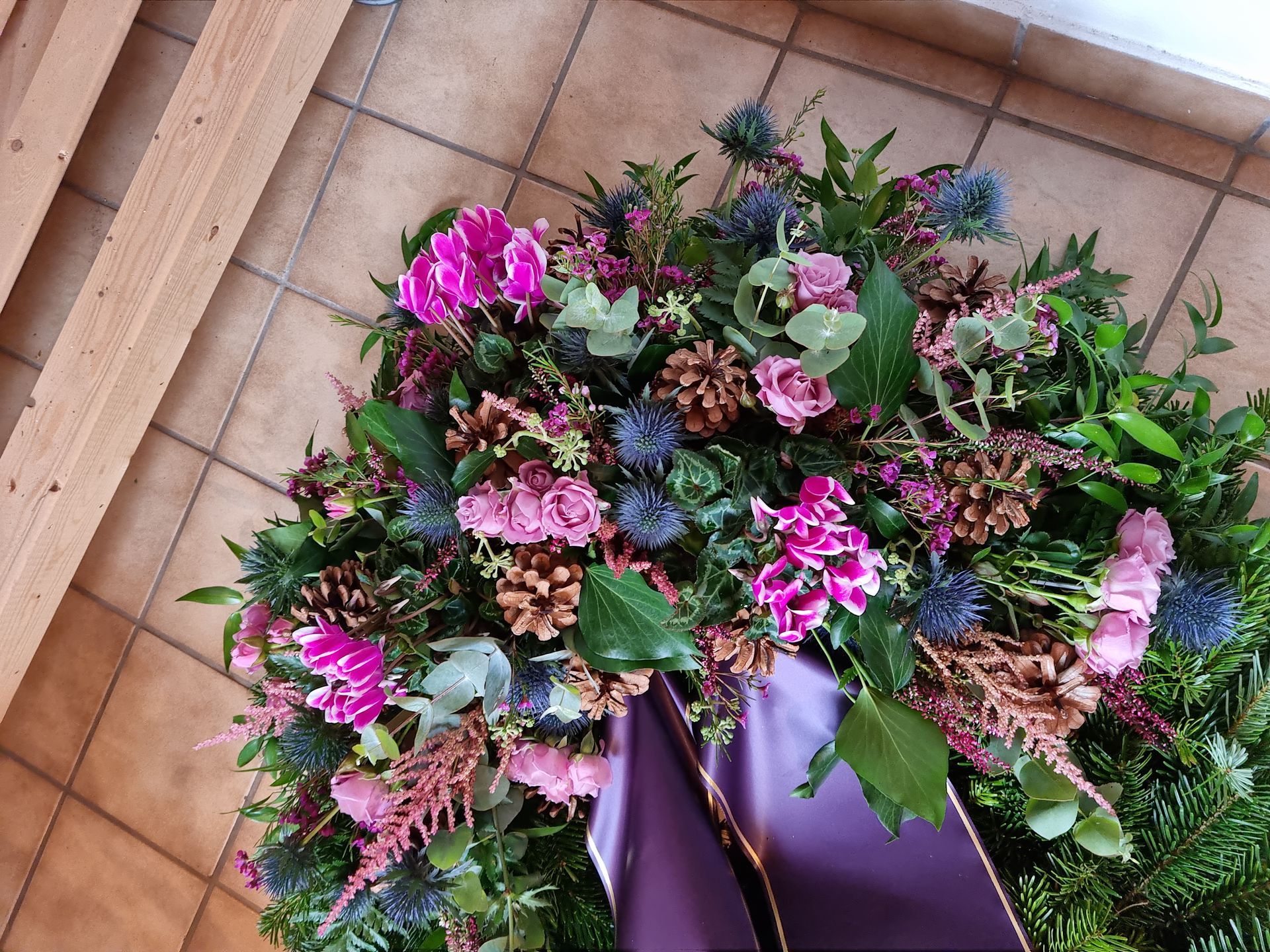 Ein Blumenkranz mit einer violetten Schleife auf einem gefliesten Boden.