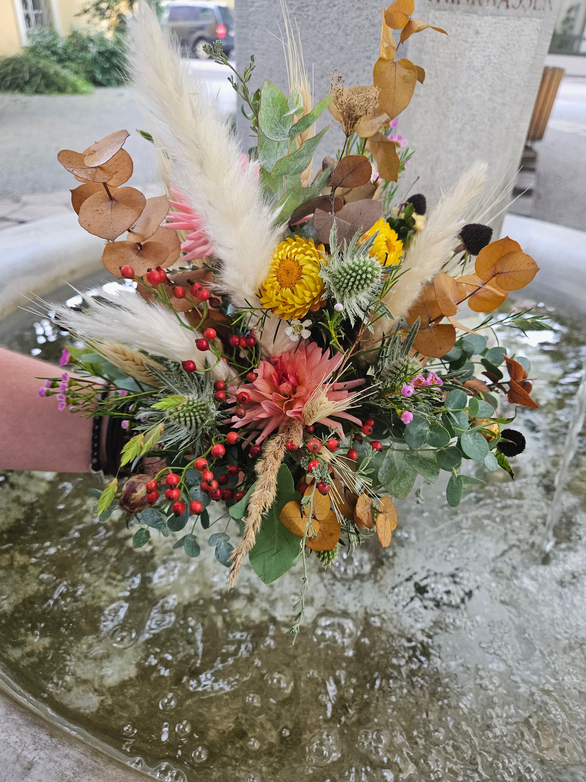 Eine Person hält einen Blumenstrauß in einem Brunnen.