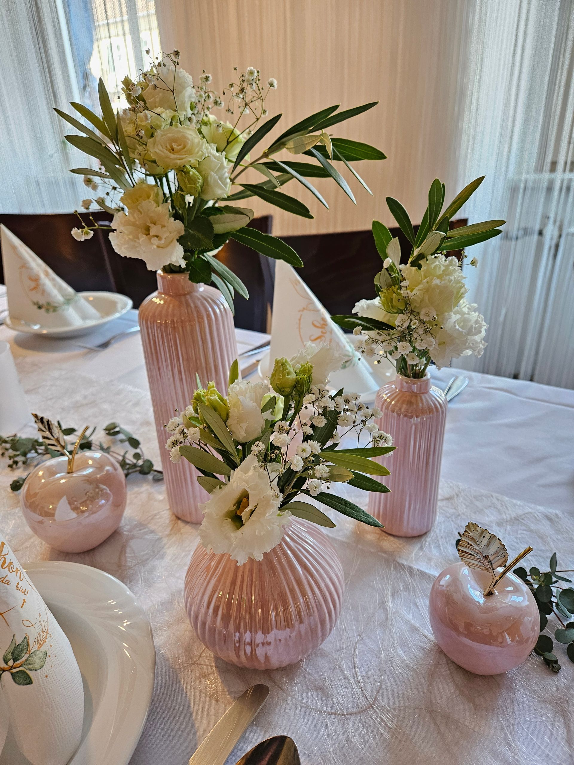 Auf einem Tisch stehen drei rosa Vasen voller Blumen.