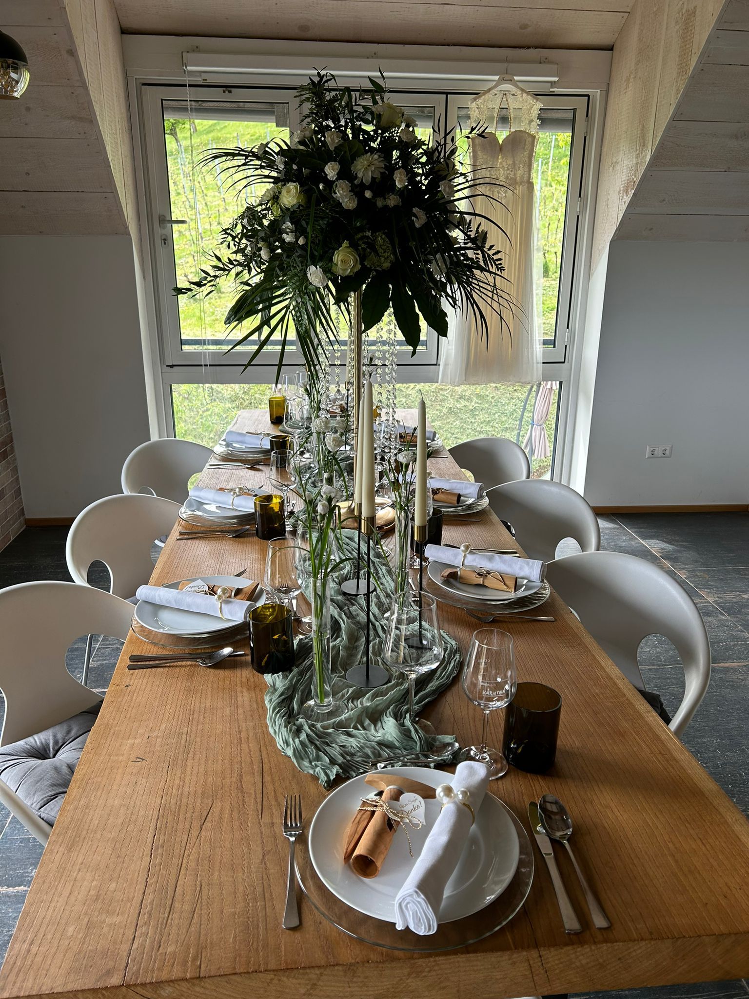 Ein langer Holztisch mit Tellern, Besteck und einer Vase mit Blumen darauf.