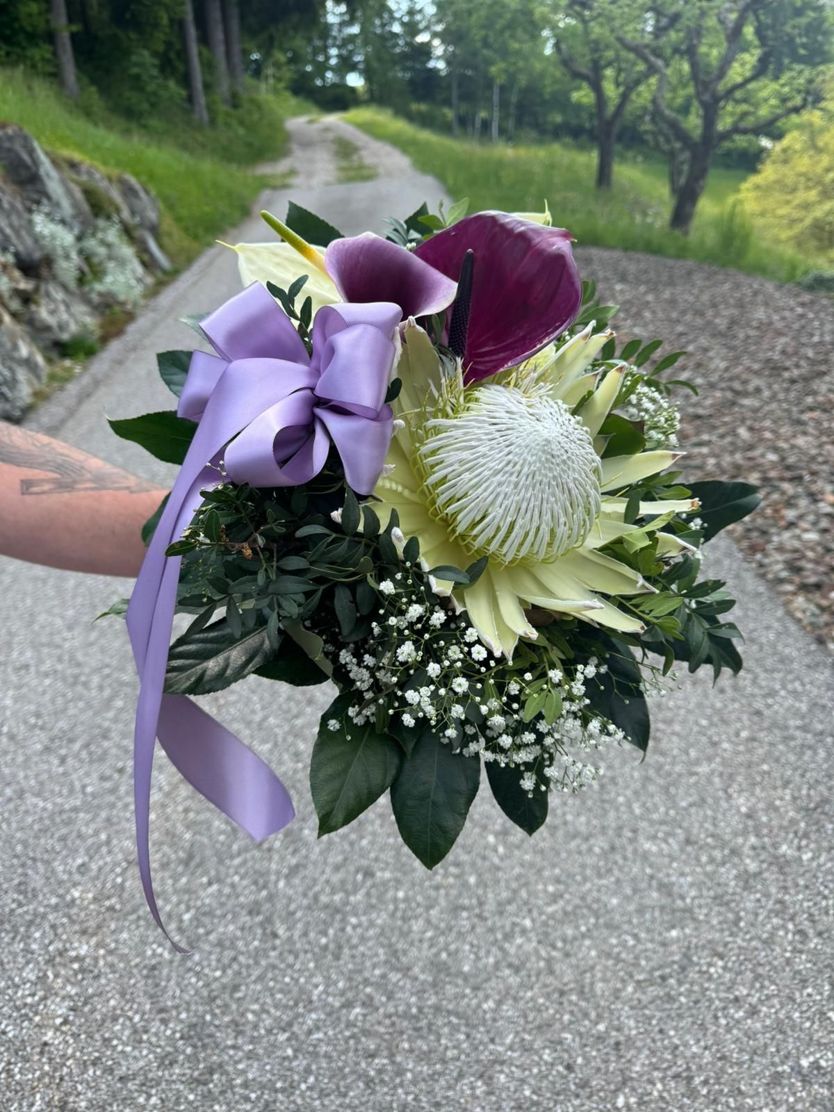 Eine Person hält einen Blumenstrauß mit einer lila Schleife.