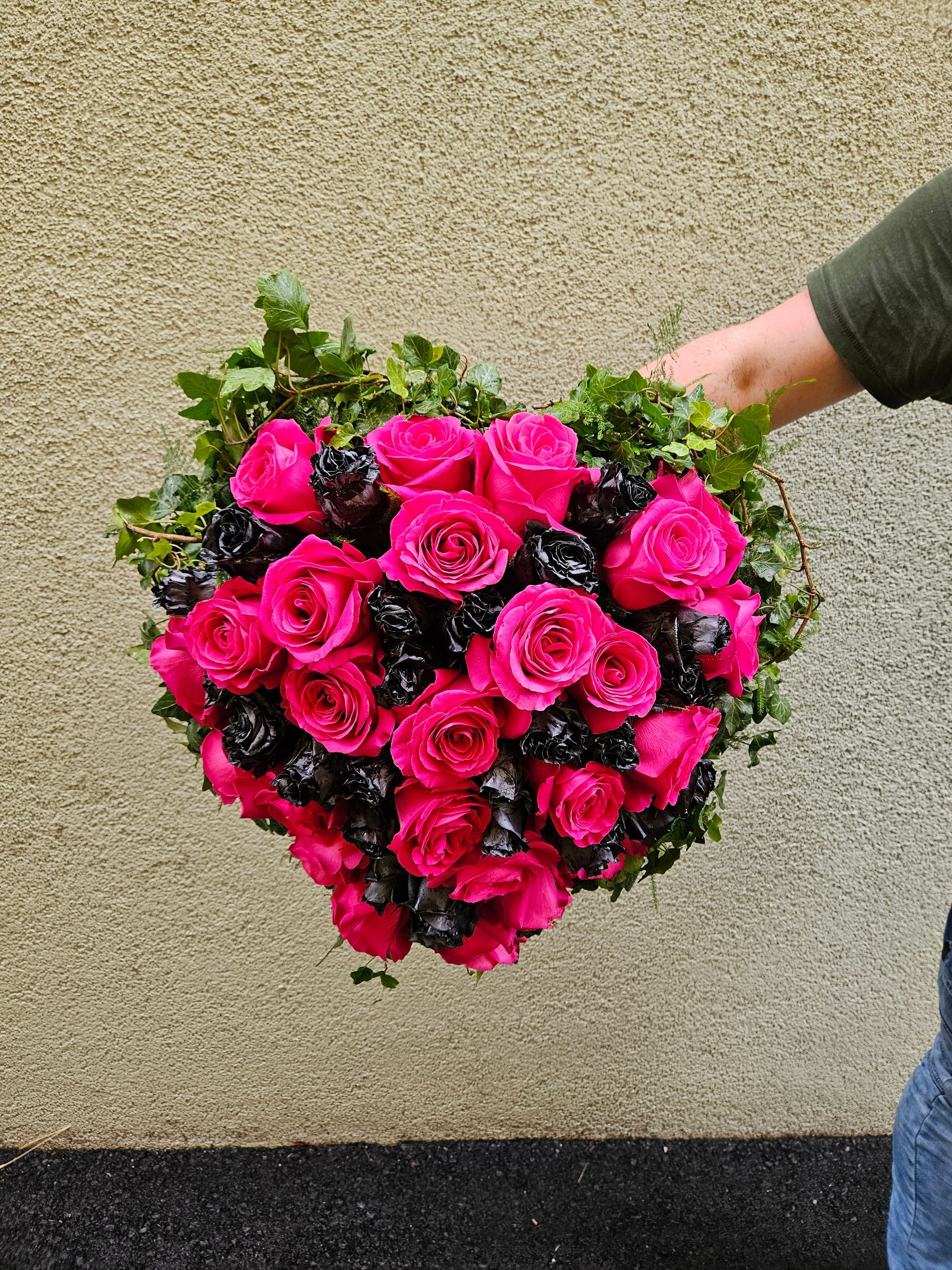 Eine Person hält einen herzförmigen Strauß aus rosa Rosen und Brombeeren.