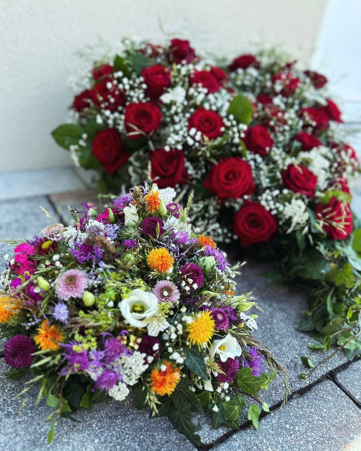 Auf einem Bürgersteig liegen zwei Blumenkränze.
