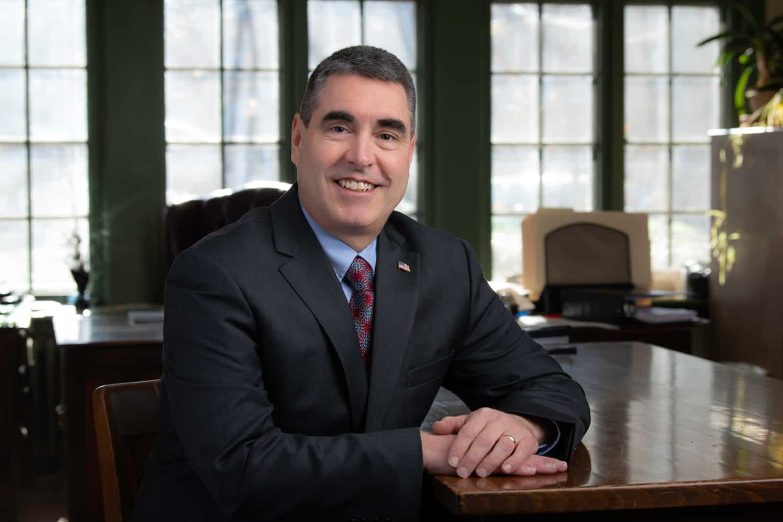 Alexander W. Scott in a suit and tie is sitting at a desk