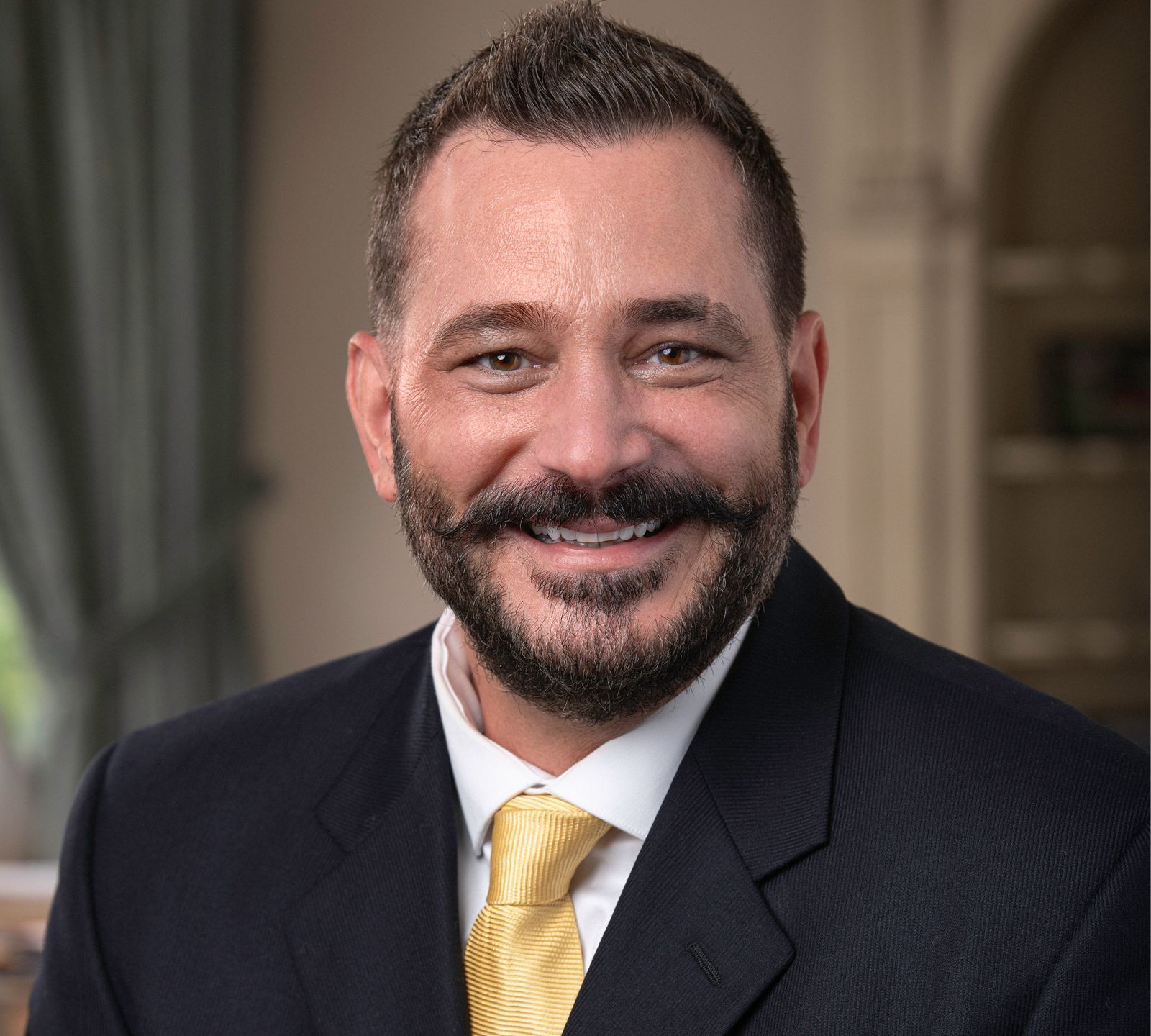 Frank A. Natoli wearing a suit and tie smiles for the camera