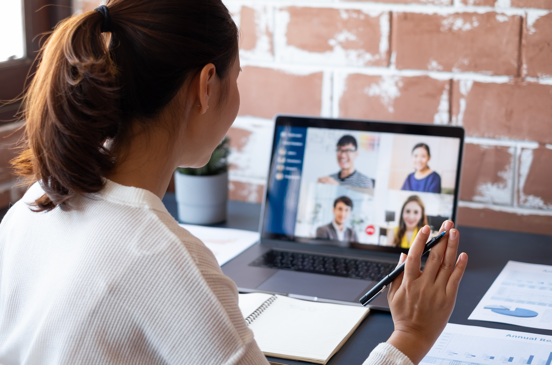 A woman is sitting at a desk using a laptop computer to have a video call with her colleagues.