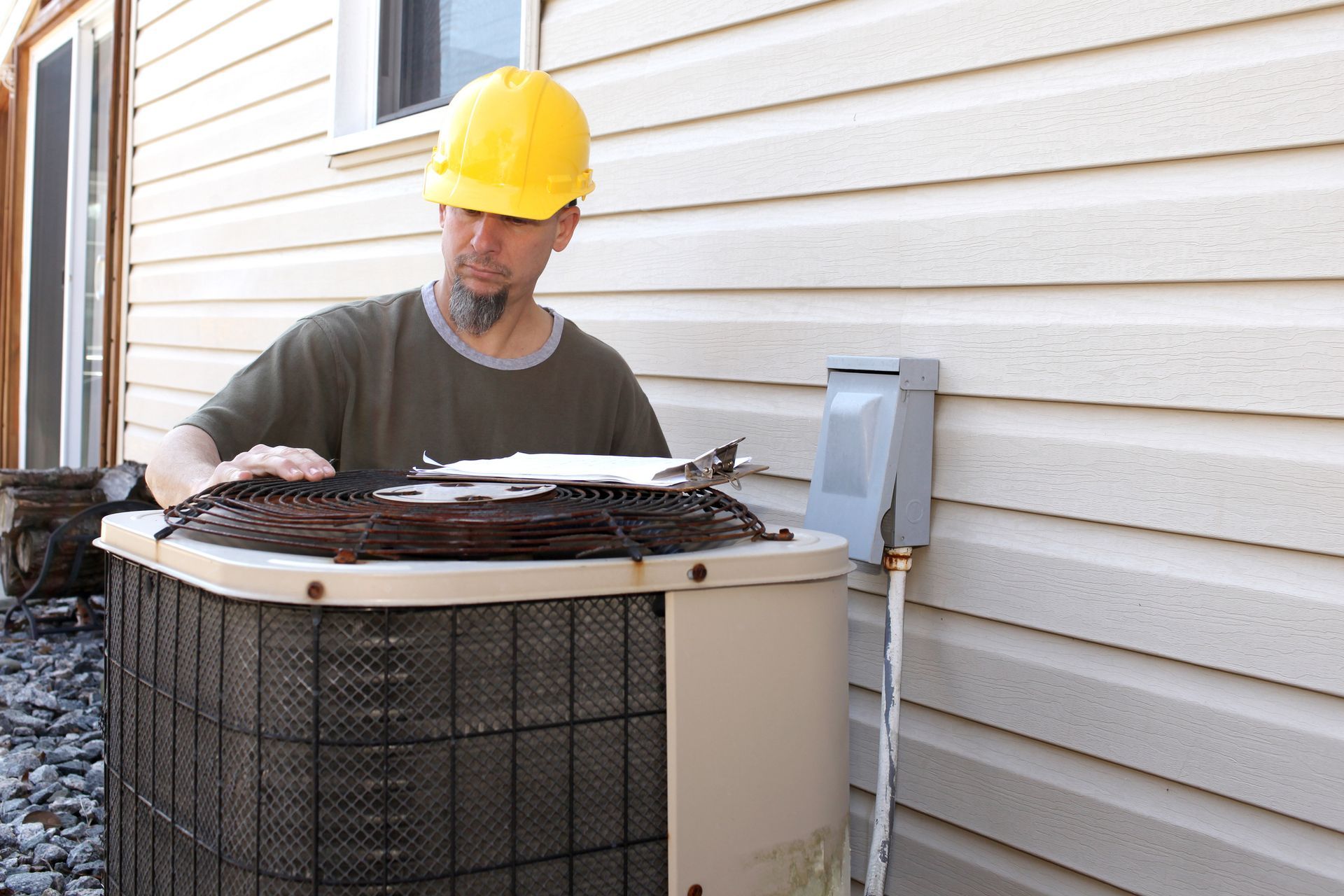 HVAC repair contractor checks an air conditioner while wearing a hard hat for safety and compliance.