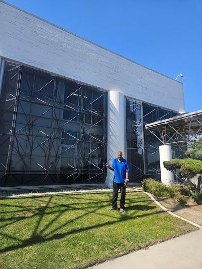 Man standing on a grassy lawn outside a modern glass-front building under a clear blue sky