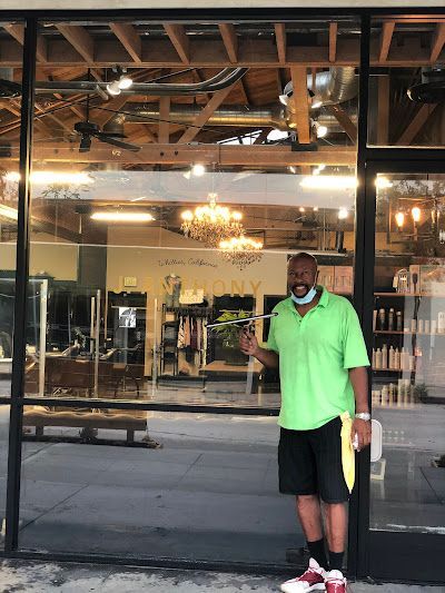 Man in green shirt standing outside a glass-front storefront with warm interior lights.