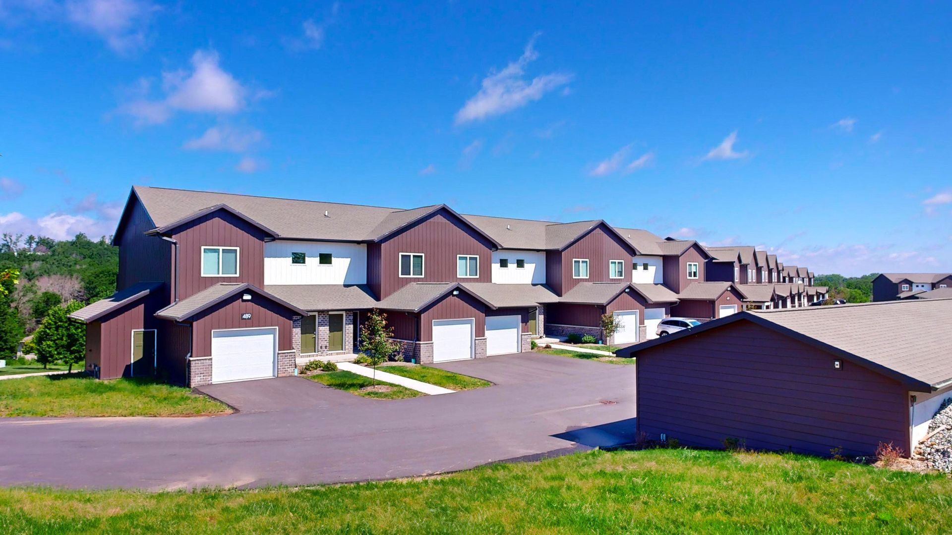 Row of beige townhouses with garages along a quiet street under a blue sky