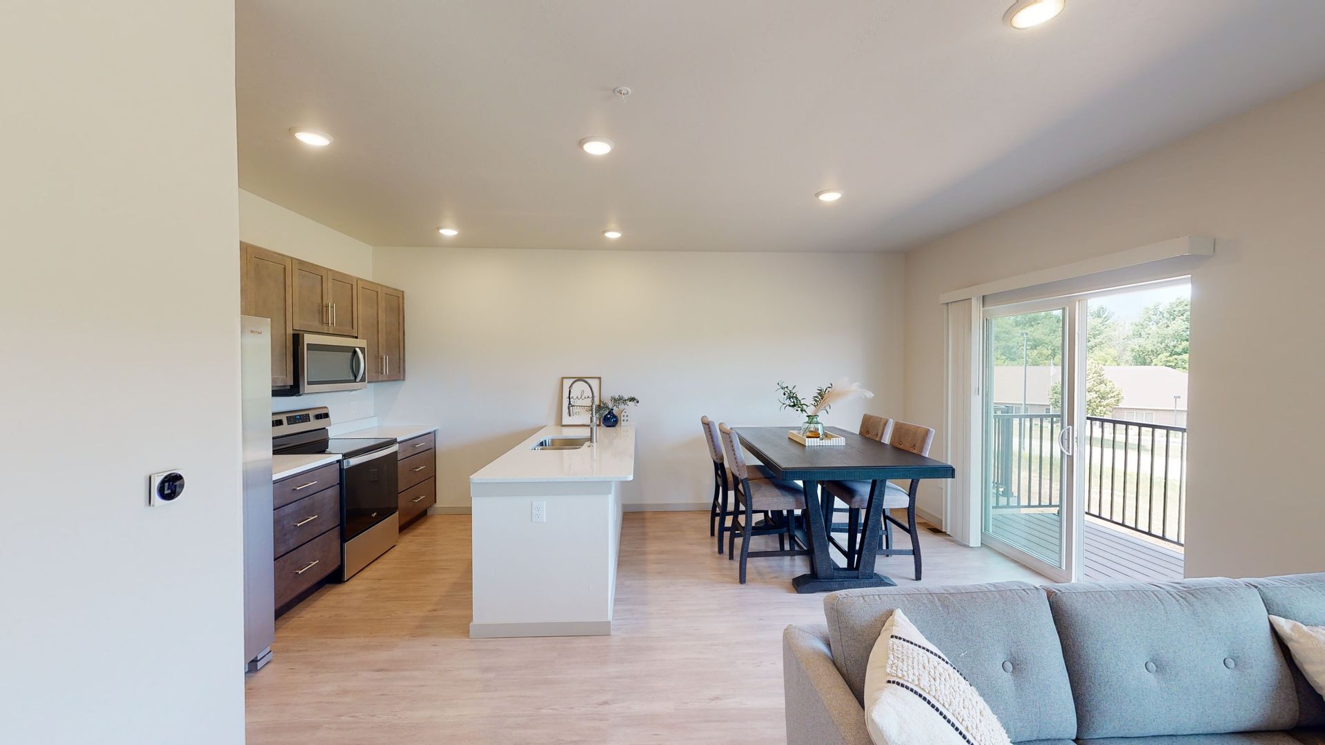 Bright open-concept kitchen and dining area with island, sofa, and sliding glass doors to a balcony