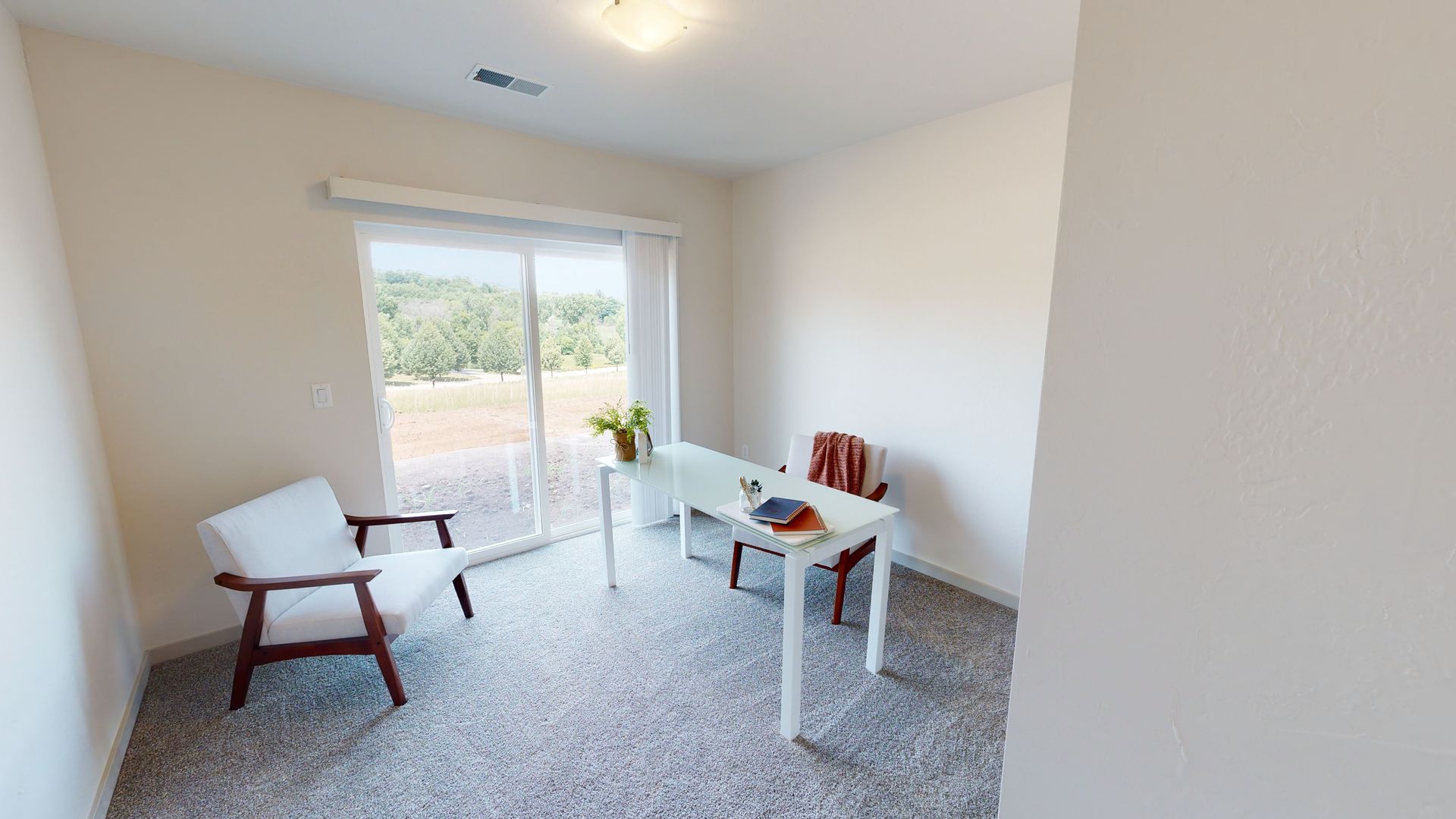 Bright empty room with two chairs, a small table, and a sliding glass door to a patio.