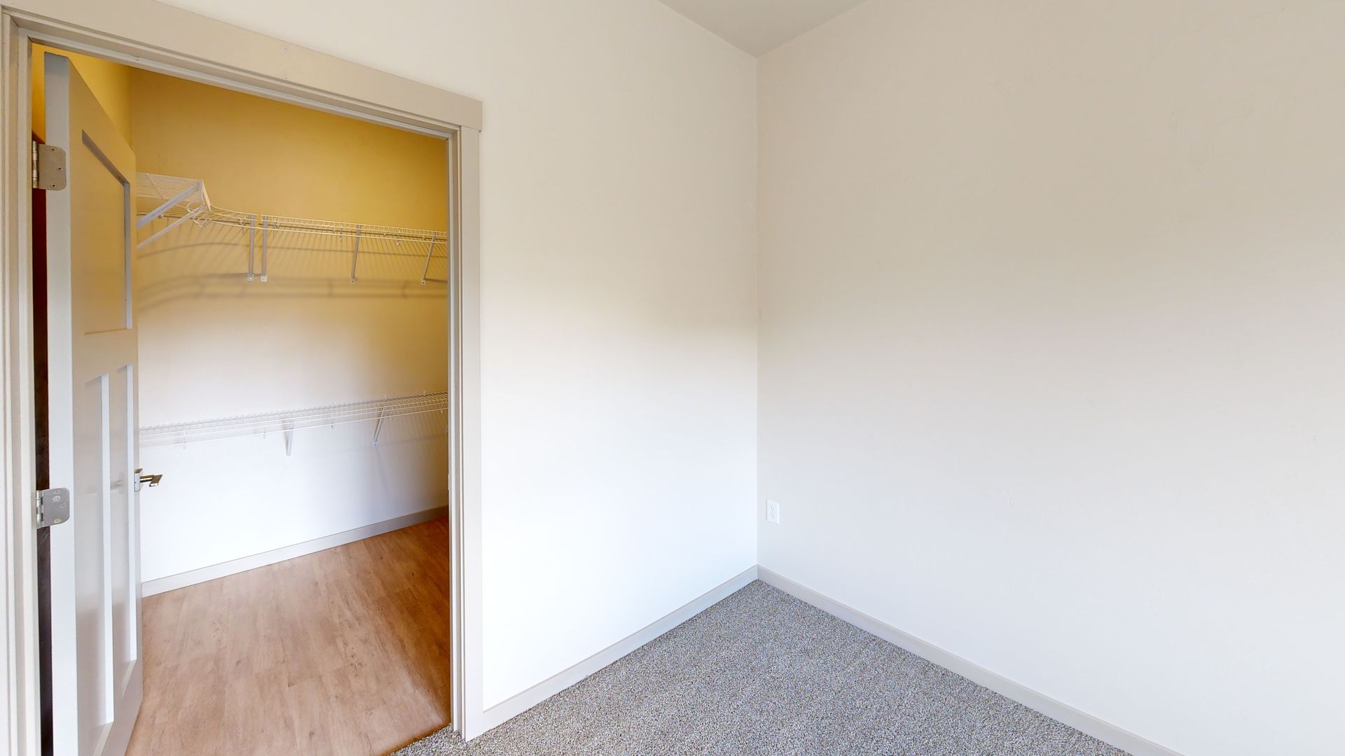 Empty bedroom with beige walls, carpet, and an open closet with wire shelving and wood floor inside
