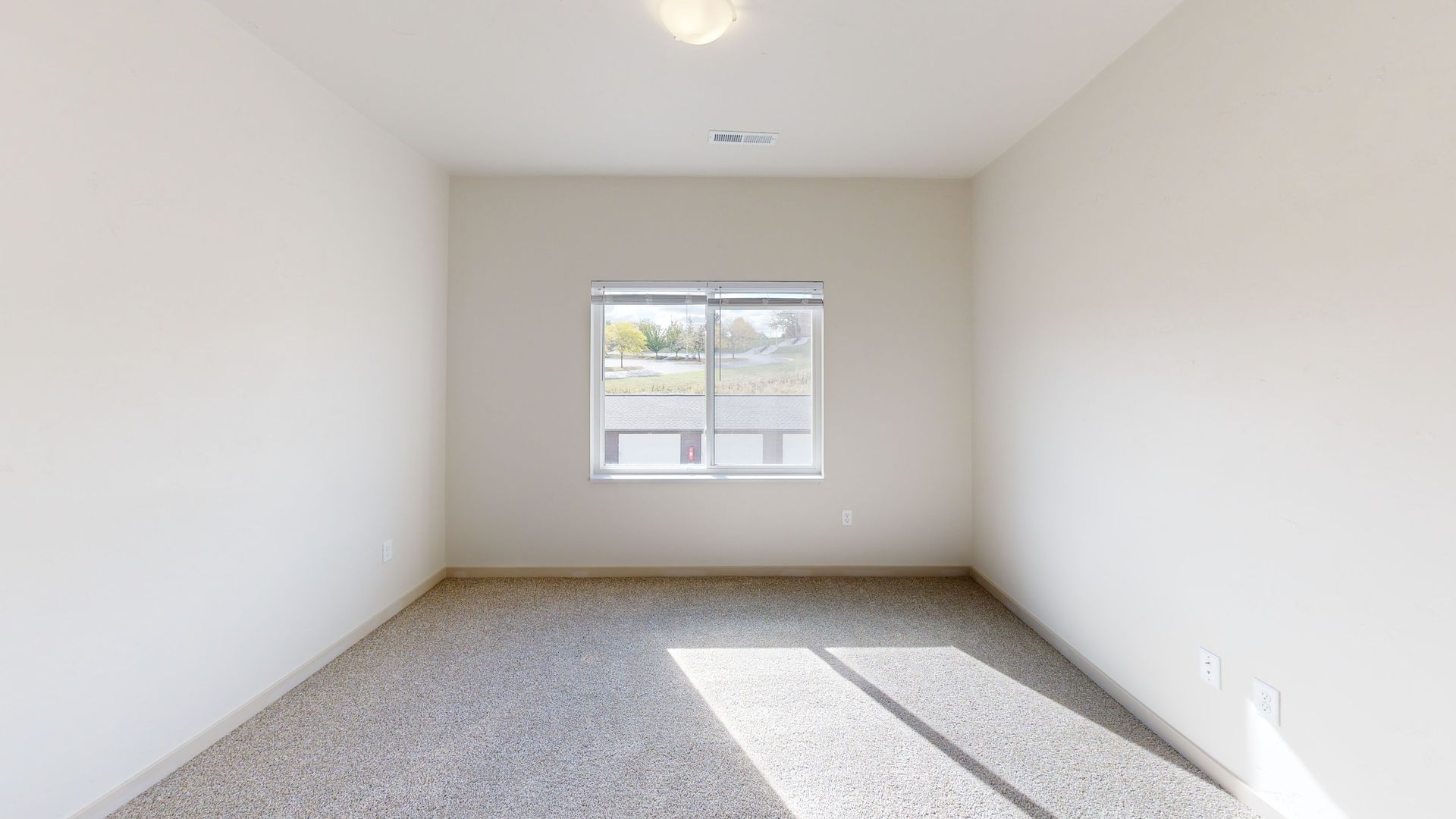 Empty white bedroom with gray carpet and a small window letting in sunlight