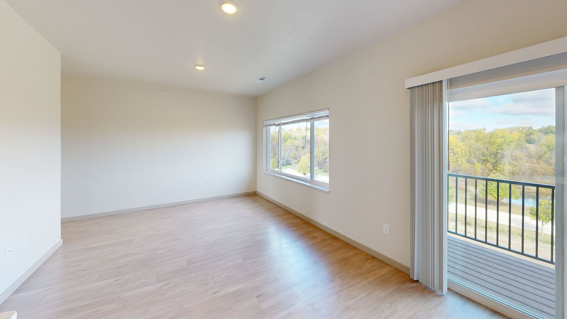 Bright empty living room with wood floors, white walls, window, and sliding glass door to a balcony.