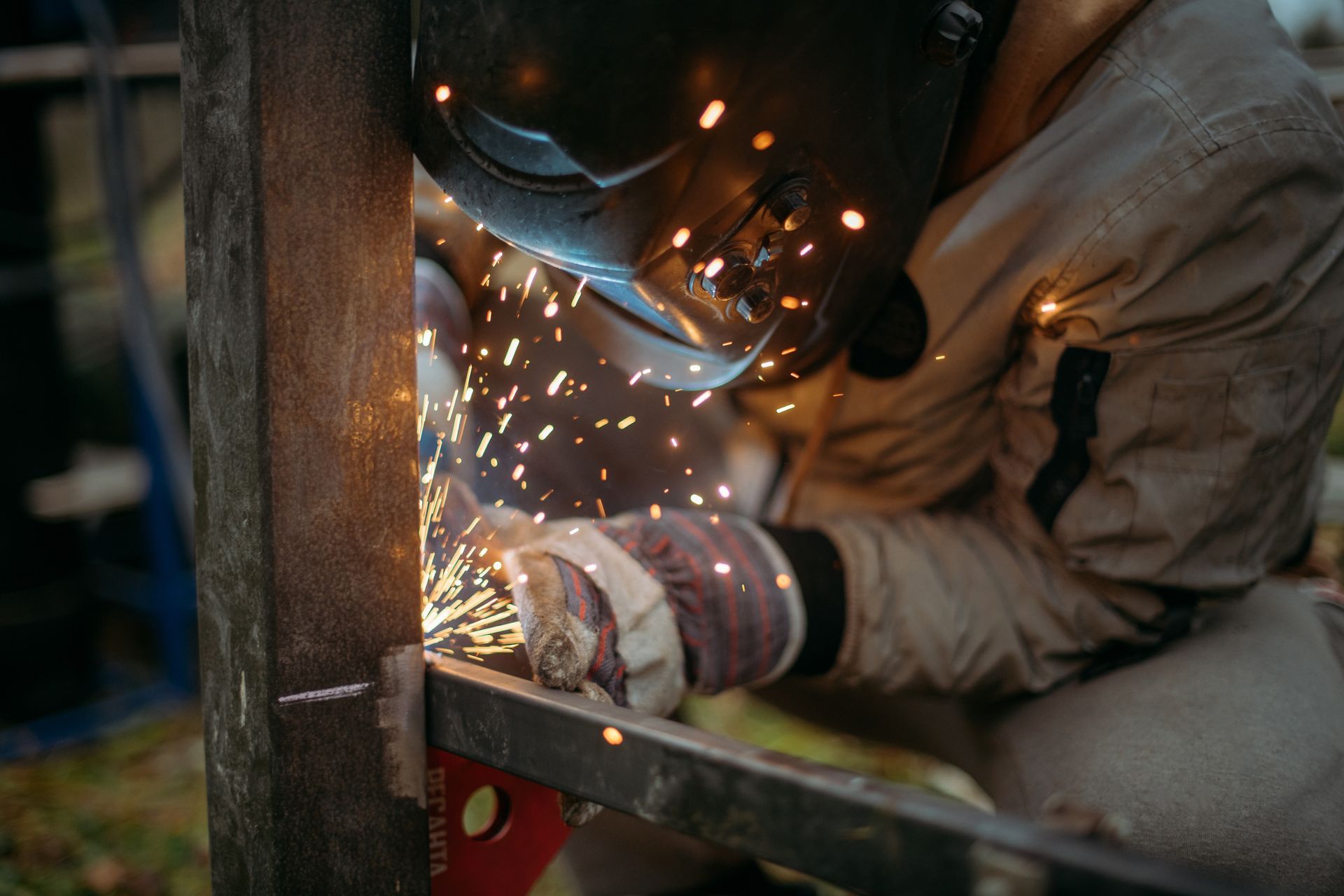Welder in protective gear sparks metal while working on a structure indoors